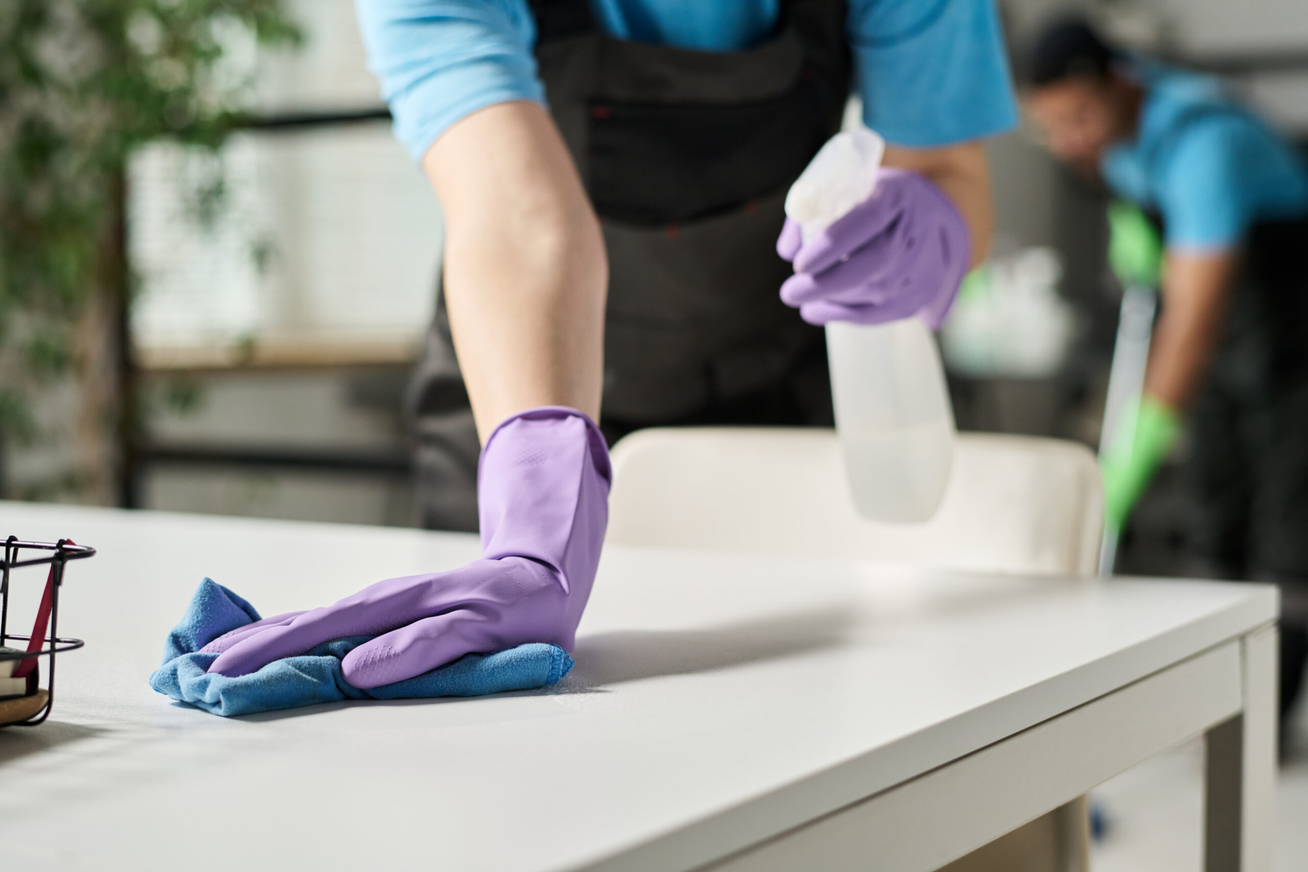 Close-up of worker in rubber gloves doing wet cleaning and wiping dust from furniture in office